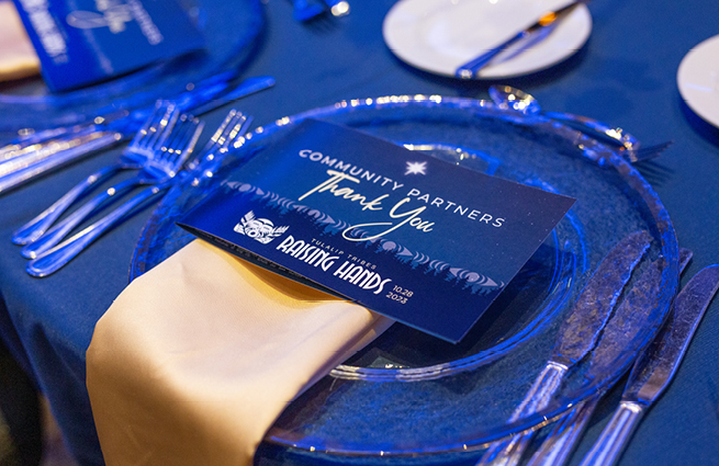 Tulalip Cares Raising Hands 2023 event shows a nice table display in a fancy blue theme with a designated thank you card on top of a nice place setting. 