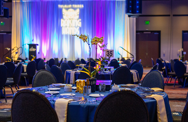 The 2023 Raising Hands event shows tables with eight chairs each in a beautiful blue colored theme at the casino in a large banquet room. 