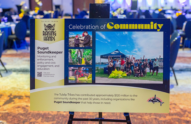 At the 2023 Raising Hands event shows a large sign on an easel for Puget Soundkeeper Celebration of Community pictures and mission statement. 