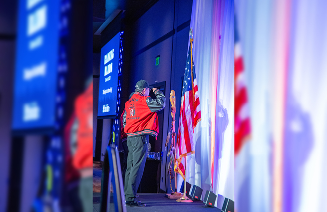 Veterans standing on stage in front of American flags, saluting with honor as patriarchs.   