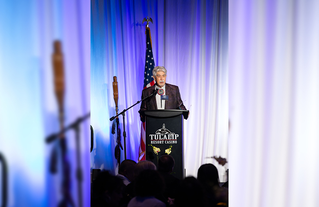 Mel Sheldon behind the 2023 Raising Hands podium, speaking to the attendees. 