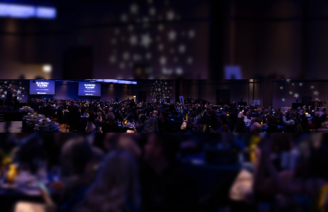 A broad view of the crowded banquet room with lights down low at the 2023 Raising Hands event.