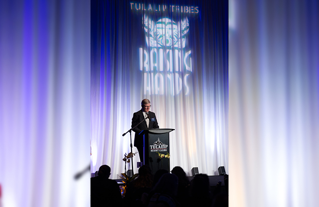 A man stands behind a podium, speaking to attendees at the 2023 Raising Hands event. 