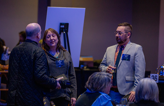 A man and woman at the 2023 Raising Hands event, visit with other guests at their table. 