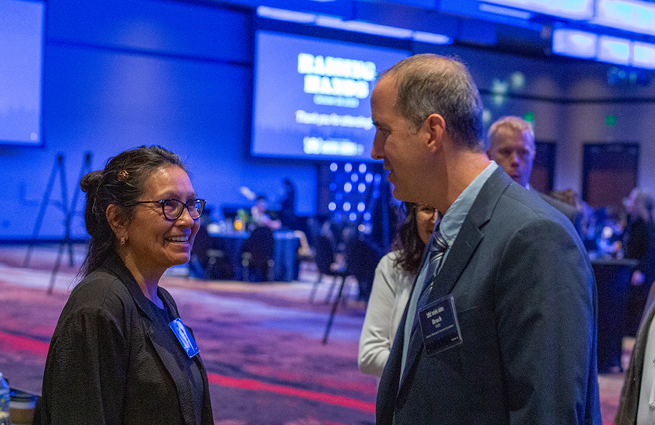 Marilyn Sheldon and a guest are standing and talking to each other at the 2023 Raising Hands event. 