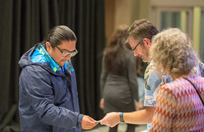 Tulalip Tribes’ 2018 Raising Hands photo of volunteer handing a guest with a blue coat a complimentary gift bag.