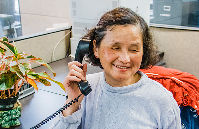 Blind woman sitting at desk on the phone at The Lighthouse for the Blind offices. 