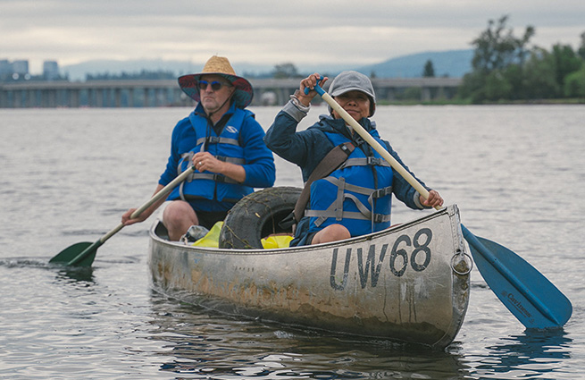 Two people wearing life jackets in a canoe, paddling in the Puget Sound. 