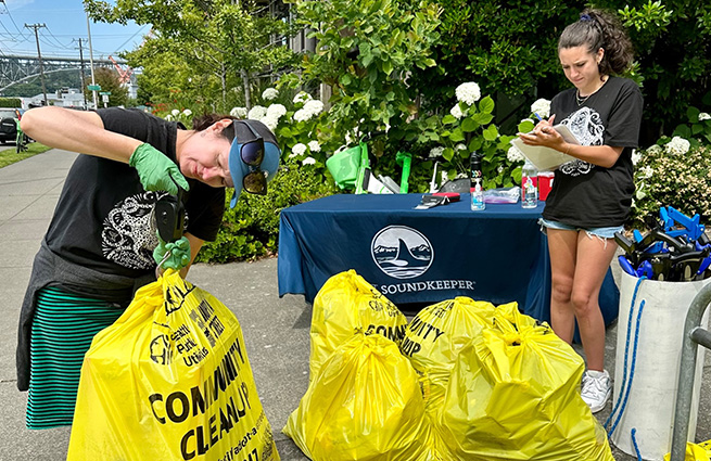 Puget Soundkeeper volunteers participating in Community Cleanup Day with several Community Cleanup bags full of liter in a pile. 