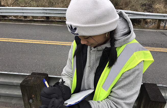 A young girl volunteers for Puget Soundkeeper making notes on a clipboard. 