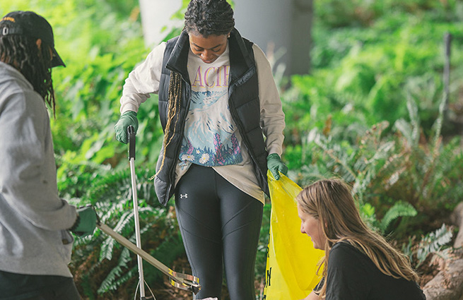 Three women together under an overpass, with grippers, cleaning up litter. 