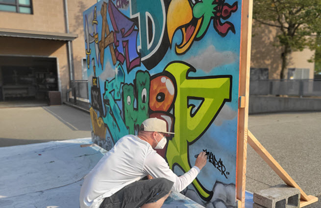 Artist signing his street art painting on a large wood canvas display