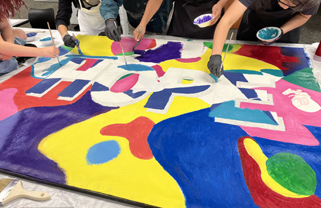 Children participating in the painting of a large artistic sign with various shapes and colors at the Schack Art Center. 